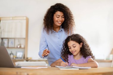 Mutlu bir anne kızına yardım ve destek olurken liseli kız ödevlerini yapıyor, yazı yazmayı öğreniyor, mutfakta iç kısımda oturuyor.