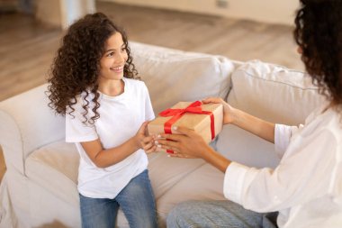 Anne kızına sürpriz hediye veriyor, doğum gününü kutluyor ve evde birlikte kanepede oturuyor.