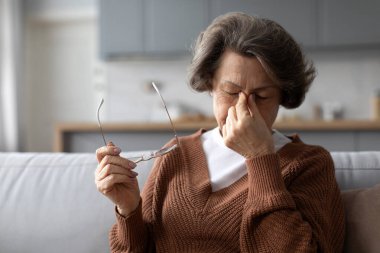Gözlüklerini çıkarmaktan yorgun düşmüş yaşlı bir kadın bulanık görme ya da baş dönmesi, görme sorunları, baş ağrısı ya da yüksek tansiyondan kaynaklanan migren sorunları yaşıyor.