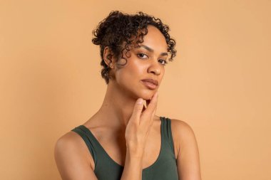 Temiz, taze, parlak tenli güzel siyah kadın bej arka planda kameraya bakıyor ve poz veriyor.