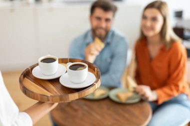 Garson elinde kahve fincanlarıyla kafe masasında bekleyen iki ziyaretçiye sıcak aromalı kahve servisi yapıyor.