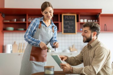 Kendi kafesinde garsonluk yapan çekici bir kadın, erkek müşteriye menüde yardım ediyor.