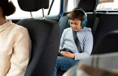 Kablosuz kulaklık takan, akıllı telefon kullanan, arka koltukta oturan bir çocuk.