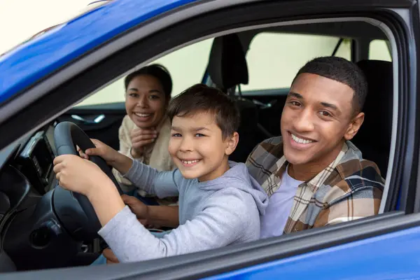 Happy preteen boy driving car, sitting with father in drivers seat smiling to camera, dad teaching son to drive