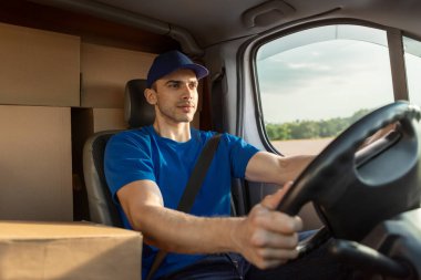 Karton kutularla dolu bir minibüsün içinde oturan ve müşterilere paket getiren ciddi bir teslimatçı.