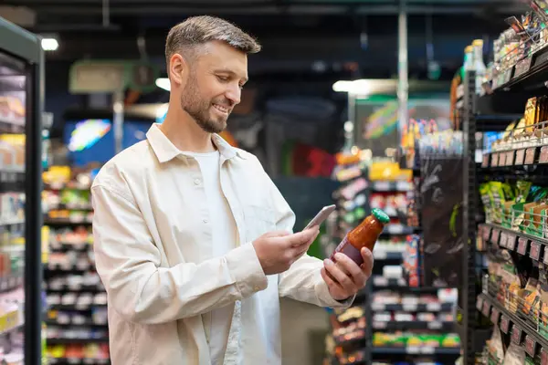 stock image Grocery shopping app. Man scanning sauce jar with smartphone buying food in modern supermarket