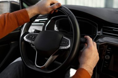 Araba koltuğunda oturan, silecekleri çalıştıran, direksiyonda el ele tutuşan adamın omuz manzarası.