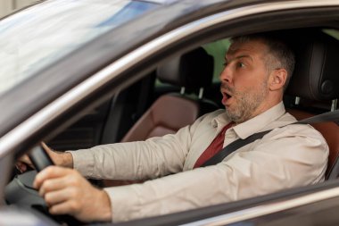 Araba kullanmanın stresi. Korkak orta yaşlı adam direksiyon başında şokta yola bakıyor, riskli bir trafik kazası geçiriyor.