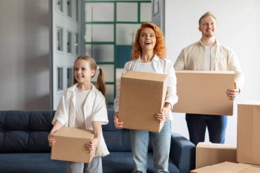 Üç kişilik heyecanlı bir aile, erkek, kadın ve kızları ellerinde karton kutular tutuyorlar. Ev taşıma kavramı