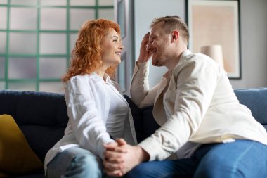 Genç ve romantik Avrupalı çift evlerinde oturup el ele tutuşup birbirlerine gülümsüyorlar.