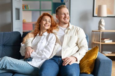 Evlilik ve sağlıklı ilişkiler. Sevgililer kucaklaşır, kanepede dinlenir, gülümseyerek, boş bir alana bakar.