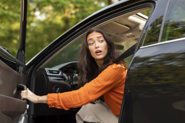 Korkmuş genç bir kadın yolda sorun yaşıyor, otomobil kapısını açıyor ve geriye bakıyor, sorun yaşıyor.