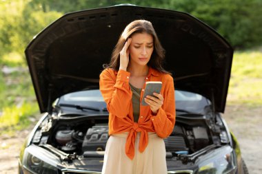 Korkmuş genç bir kadın arızalı bir arabada duruyor ve cep telefonu kullanıyor, arama yapıyor ve yardım için mesaj yazıyor.