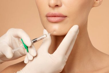 Kadın çenesinin yanında şırınga tutan kozmetik uzmanı çene şeklini düzeltmek için doldurulan güzellik enjeksiyonları, çenenin çevresindeki prosedürler.