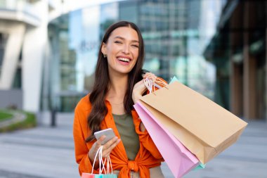 Büyük satışlar. Alışveriş merkezinin yakınındaki caddede, alışveriş çantaları ve akıllı telefonları olan mutlu, genç Avrupalı bir bayan. Dükkandan reklam ve teklif