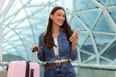 Seyahat başvurusu. Havaalanında ya da tren istasyonunda bavulla beklerken akıllı telefon kullanan bir kadın biletleri telefonla kontrol ediyor.