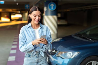 Mutlu bir kadın yeraltı otoparkında yürüyor, arabasından uzaklaşıyor, alışveriş merkezine geliyor ve cep telefonunu kullanıyor.