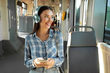 İyi yolculuklar. Modern tramvayda oturan ve kablosuz kulaklık takan bir bayan. Rahat şehir ulaşımı kavramı