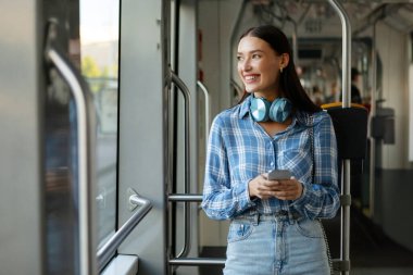 Tramvaydaki kadın, modern tramvayın içindeki yolculuğunun keyfini çıkarıyor, yana bakıyor ve gülümsüyor. Gidiş-dönüş ve bağlantı