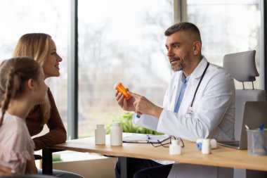 Tıbbi bir randevu. Erkek doktor çocuk için ilaç tedavisi ve haplı kavanoz öneriyor.