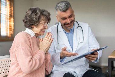 İlgilenen erkek doktor konuşuyor ve yaşlı kadın hastaya danışıyor. Doktor üst düzey kadın müşteriye düzenli muayene yapıyor.
