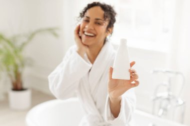 Saç şampuanı ya da duş jeli olan şeker şişesi, bornozlu siyahi kadın fotokopi alanı olan nemlendirici losyon kozmetik ürünü gösteriyor.