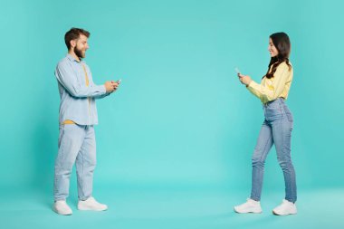 Ellerinde akıllı telefonlar olan kadın ve erkek birbirlerinin yanından geçiyorlar, turkuaz stüdyo arka planına karşı duran çift, fotokopi alanı olan kenar görüş.