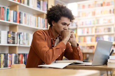 Zeki odaklı siyah erkek öğrenci, masada üniversite kütüphanesinde oturuyor, derse ya da sınava hazırlanıyor, bilgi ve öğrenim kavramına.