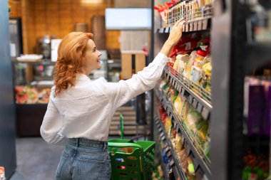 Kadın tüketici süpermarketten alışveriş yapıyor, raftan gıda ürünü seçiyor, marketten alışveriş yapıyor.