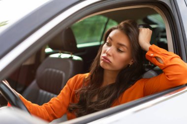 Zor bir trafik sıkışıklığında beklemekten yorgun düşmüş, direksiyon tutan Avrupalı bir kadın.