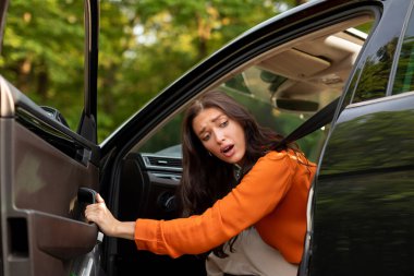 Şok olmuş genç bayan yolda sorun yaşıyor, otomobil kapısını açıyor ve patlak lastiğe bakıyor.