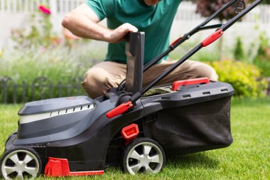 Yeşil bahçede çim biçen ve çim biçerken elektrikli çim biçme makinesini kontrol eden erkek işçi. Bahçıvan bahçeyi buduyor.