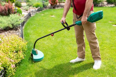 Bahçesindeki çimleri biçmek için elektrikli çim biçme makinesi kullanan tanınmamış bir bahçıvan. Bahçede bahçe bakımı