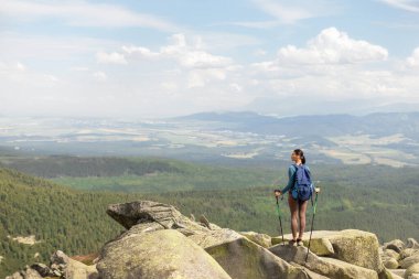 Sırt çantalı ve tepenin üstünde yürüyüş direkleri olan kadın turist dağların manzarasının keyfini çıkarıyor.