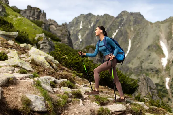 Sırt çantalı, dağlarda yürüyüş yapan, yürüyüş direkleri kullanan ve güzel manzaranın tadını çıkaran aktif genç bir kadın.