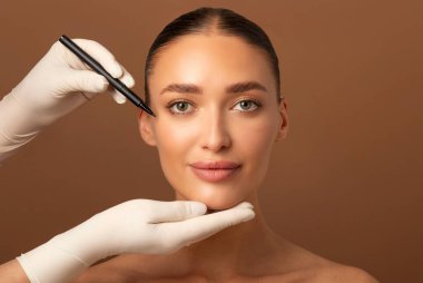 Güzellik uzmanı doktor genç kadın yüzüne kalemle çizgiler çiziyor Avrupalı kadın klinikte estetik ameliyat oluyor.
