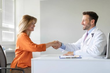 Klinikteki ilk muayenede kadın hastayla el sıkışan dost canlısı erkek pratisyen hekim, kadın müşteriyle el sıkışan adam, sağlık sigortası anlaşması, yan görüş.