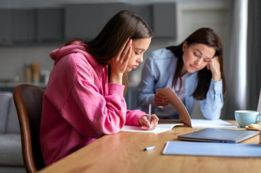 Üzgün anne ve kız evde çalışıyor, kız okul ödevleri yapıyor, zor iş, rutin sıkıcı ev ödevleri, katı anne kontrollü okul kızı.