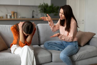 Depresyondaki genç kız kulaklarını kapatıyor, annesini dinliyor ve ağlıyor, kanepede oturan dizginsiz kadın kızına sesini yükseltiyor.