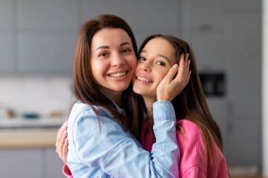 Genç kızıyla kucaklaşan mutlu bir anne. Yüzlerine dokunan, sıcak aile anlarından hoşlanan, sevgisini ifade eden, şefkatini ifade eden bir çocuk.