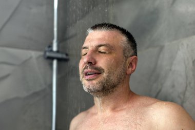 Rahatlamış orta yaşlı bir adam sabahları soğuk duş alıyor. Evdeki banyoda düşen suyun altında duruyor.