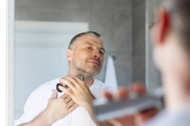 Avrupalı bir adam kalın sakalını kesiyor ya da banyo içinde elektrikli tıraş makinesiyle boynu traş ediyor. Sakal bakımı araçları kavramı