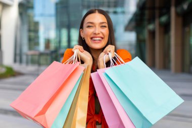 Bir sürü alışveriş çantasıyla poz veren mutlu Avrupalı kadın portresi, elinde renkli kağıt paketler, hafta sonu satışlarının keyfini çıkarıyor. Ticaret ve indirimler