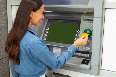 Para çekmek için ATM kullanan, kredi kartı kullanan, kartından para çeken ve dışarıda para transferleri yapan bir kadın.
