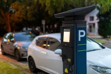 Sokakta park etmiş arabaların yanındaki modern parkmetre. Kentsel alan kavramında park cezası