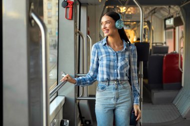 Otobüste tek başına duran ve kulaklıkla müzik dinleyen bir bayan, toplu taşıma aracının keyfini çıkarın.