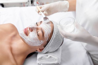 Profesyonel kozmetik uzmanı hastaların yüzüne yüz maskesi takıyor. Nemlendirici, temizlik ve yüz bakımı