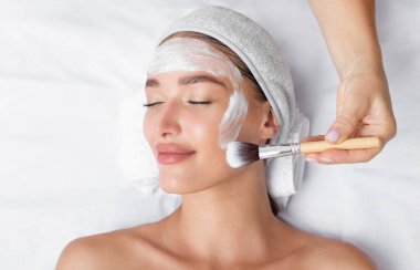 Güzellik salonunda ya da güzellik salonunda uzanan temiz cilt için rahatlatıcı kaolin kil kozmetik maskeyle kaplı genç bir kadın.
