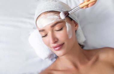 Güzeller güzeli genç bir kadın kozmetolog randevusunda güzellik salonunda uzanırken yüz maskesi takmaktan zevk alır.