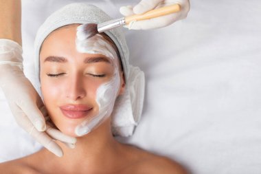 Yüz güzelliği tedavisi. Güzeller güzeli bir kadın kaplıca salonunda maske takıyor. Kozmetik uzmanı beyaz maske takıyor.